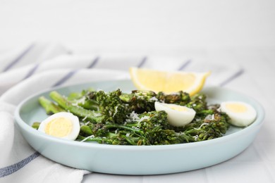 Tasty cooked broccolini with cheese, quail eggs and lemon on table, closeup