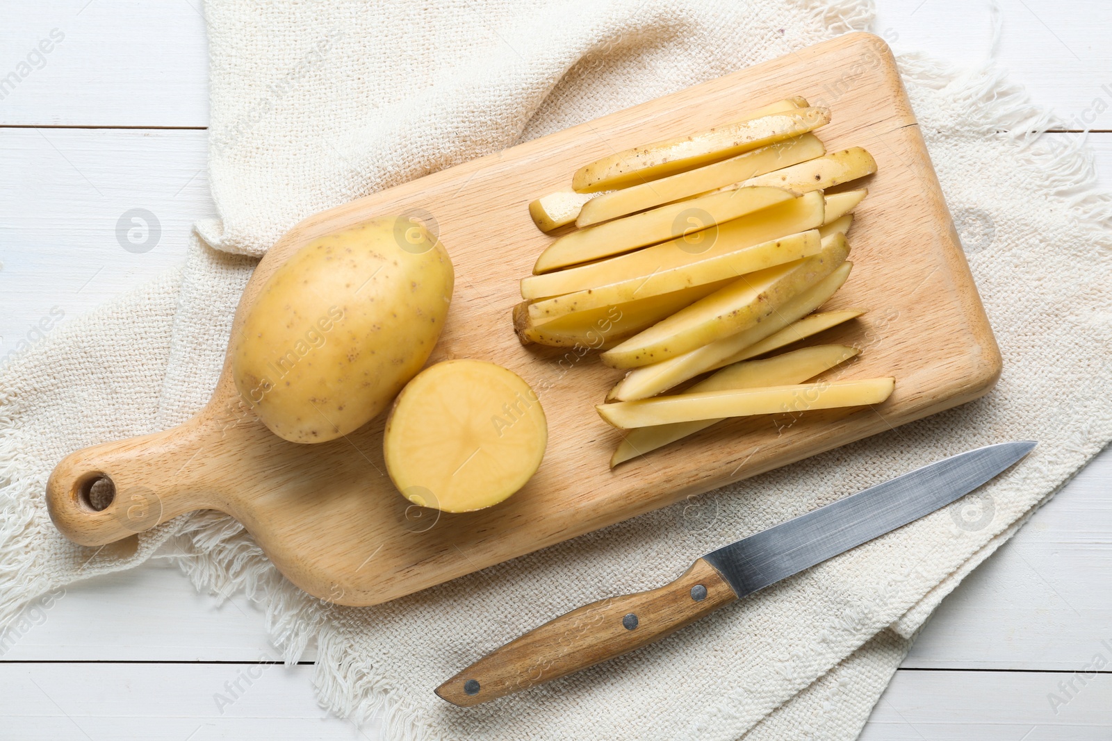 Photo of Whole and cut potatoes with knife on white wooden table, top view. Cooking delicious french fries