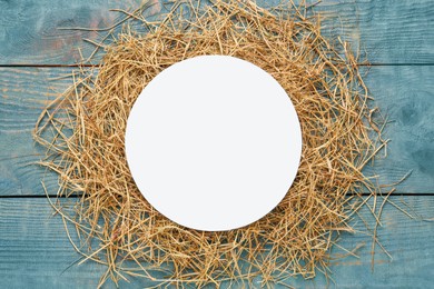 Photo of Heap of dried hay and blank card on light blue wooden background, flat lay. Space for text