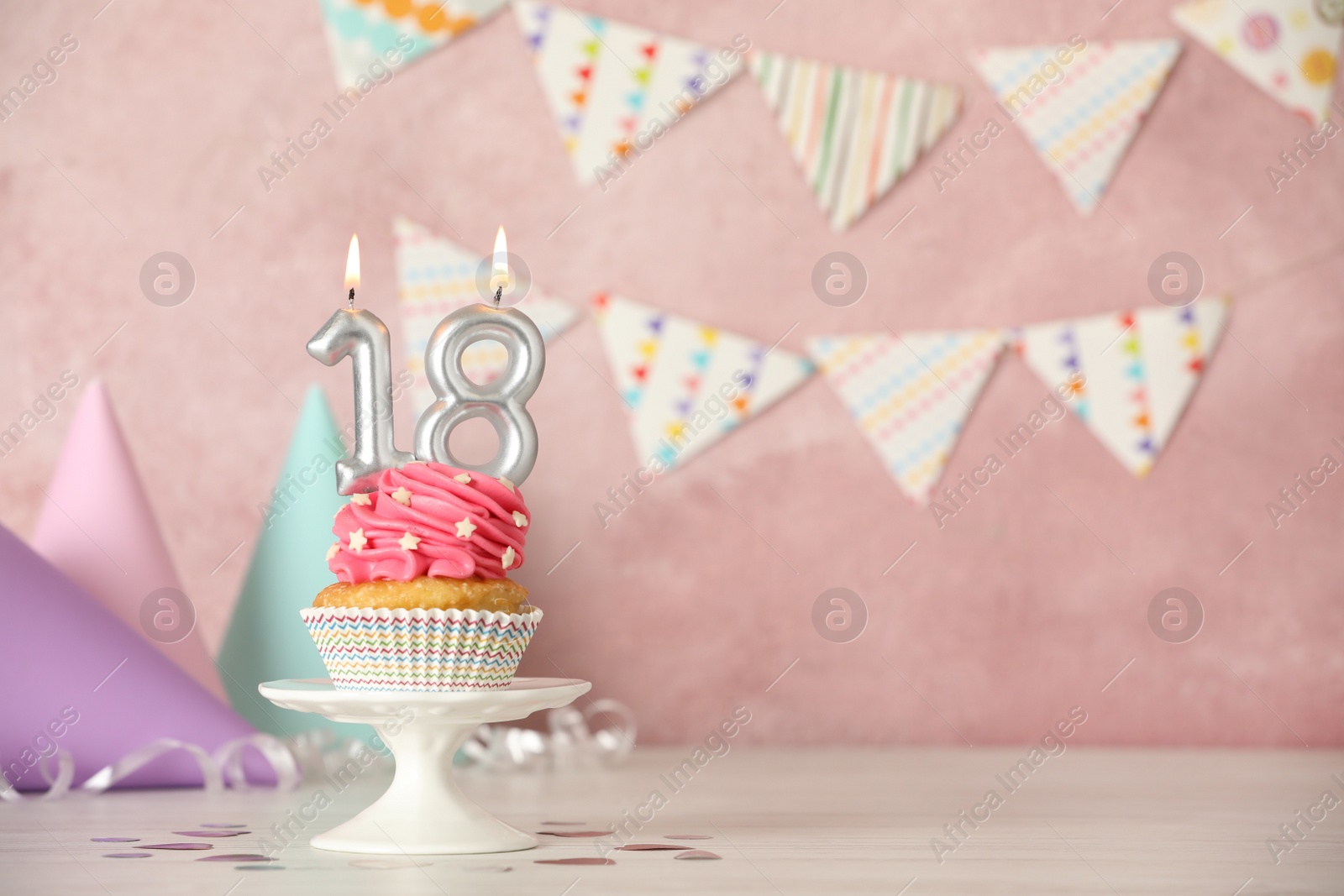 Photo of 18th birthday, coming of age party. Delicious cupcake with number shaped candles on white table, space for text