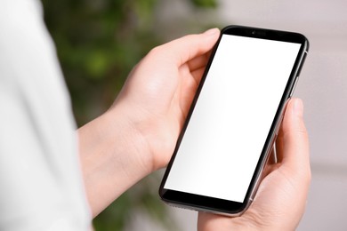 Woman holding smartphone with blank screen on blurred background, closeup. Mockup for design