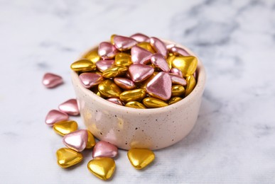 Photo of Bowl and delicious heart shaped candies on white marble table