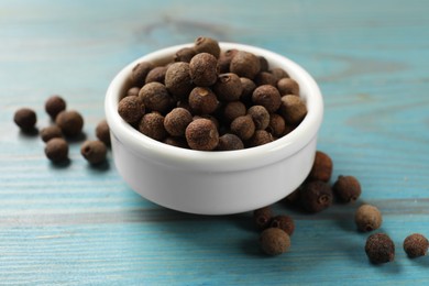 Photo of Aromatic allspice pepper grains in bowl on light blue wooden table, closeup