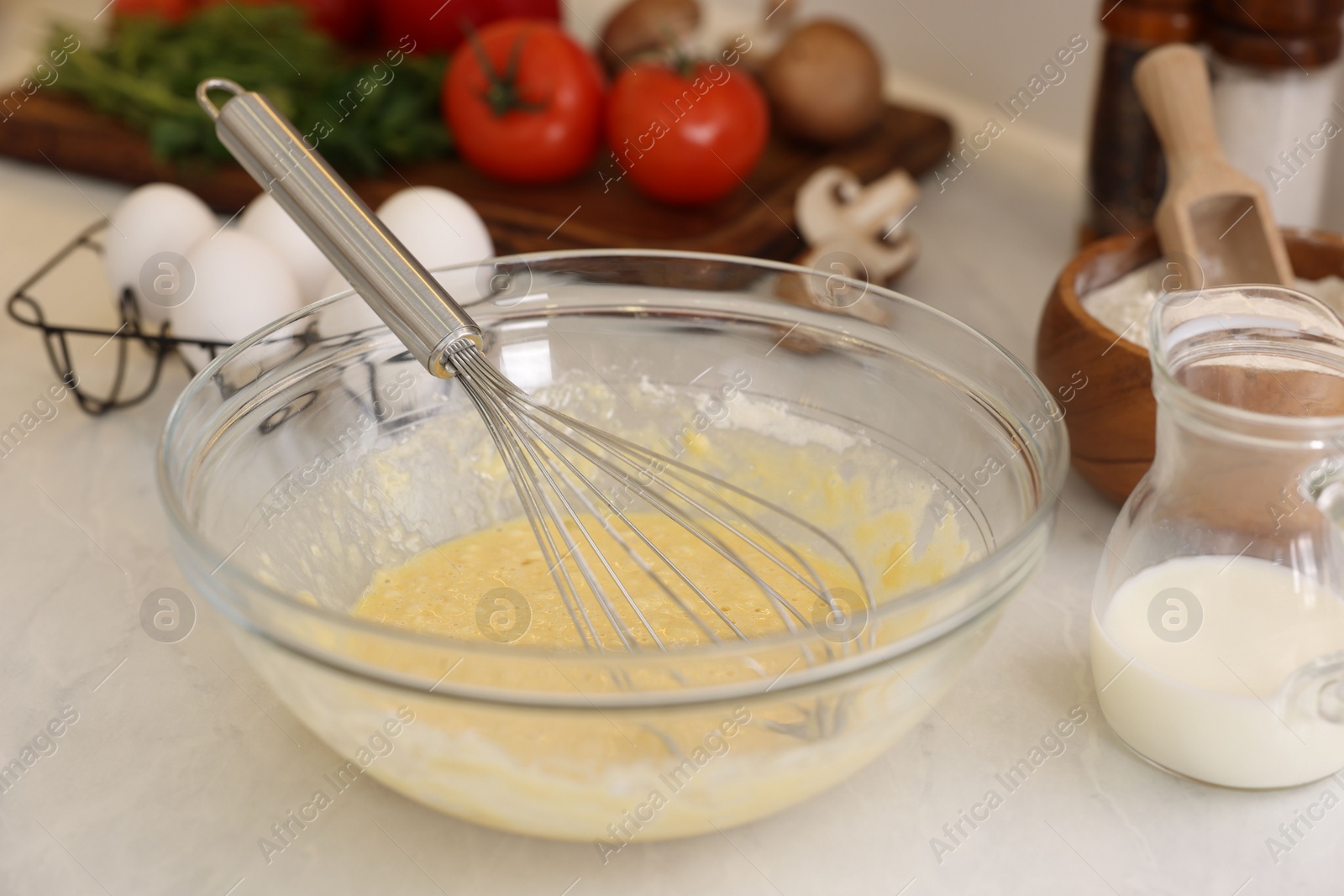 Photo of Metal whisk, cream in bowl and different products on light table