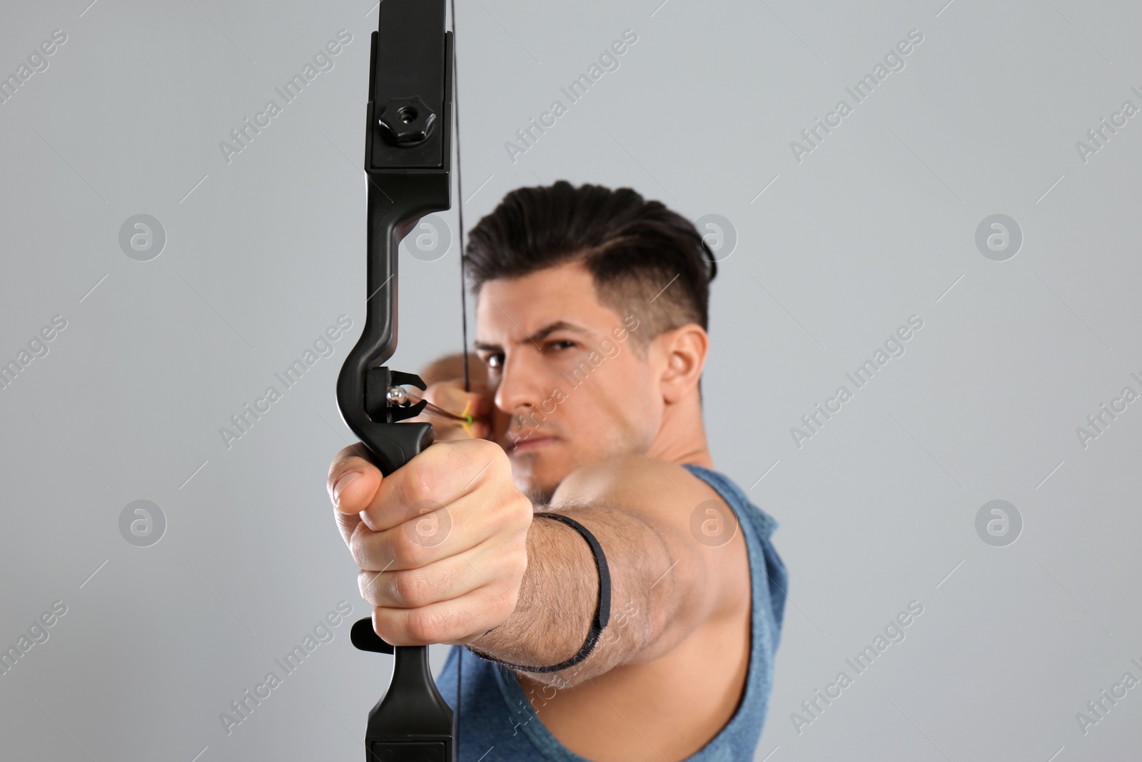 Photo of Man with bow and arrow practicing archery against light grey background, focus on hand