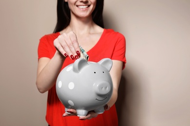Woman putting money into piggy bank on color background, closeup