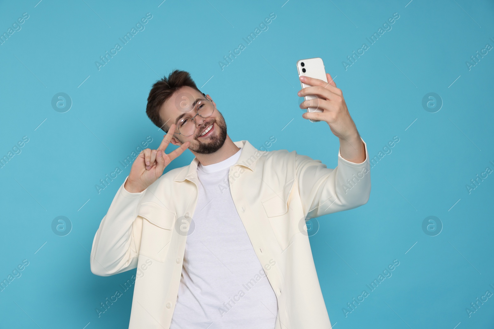 Photo of Handsome man in white jacket and eyeglasses taking selfie on light blue background