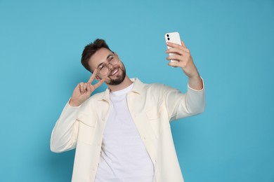 Handsome man in white jacket and eyeglasses taking selfie on light blue background