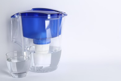 Filter jug and glass with purified water on white background. Space for text