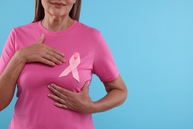 Woman with pink ribbon on light blue background, closeup and space for text. Breast cancer awareness