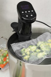 Sous vide cooker and vacuum packed broccoli in pot on white table. Thermal immersion circulator
