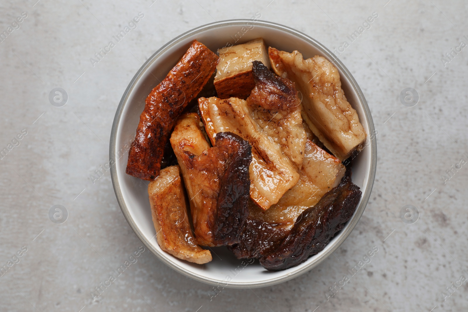 Photo of Bowl with tasty fried pork fatback slices on grey table, top view