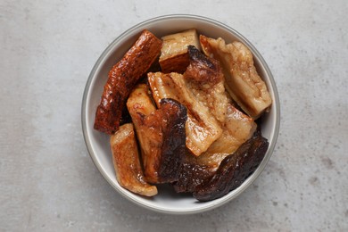 Photo of Bowl with tasty fried pork fatback slices on grey table, top view