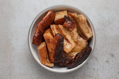 Bowl with tasty fried pork fatback slices on grey table, top view