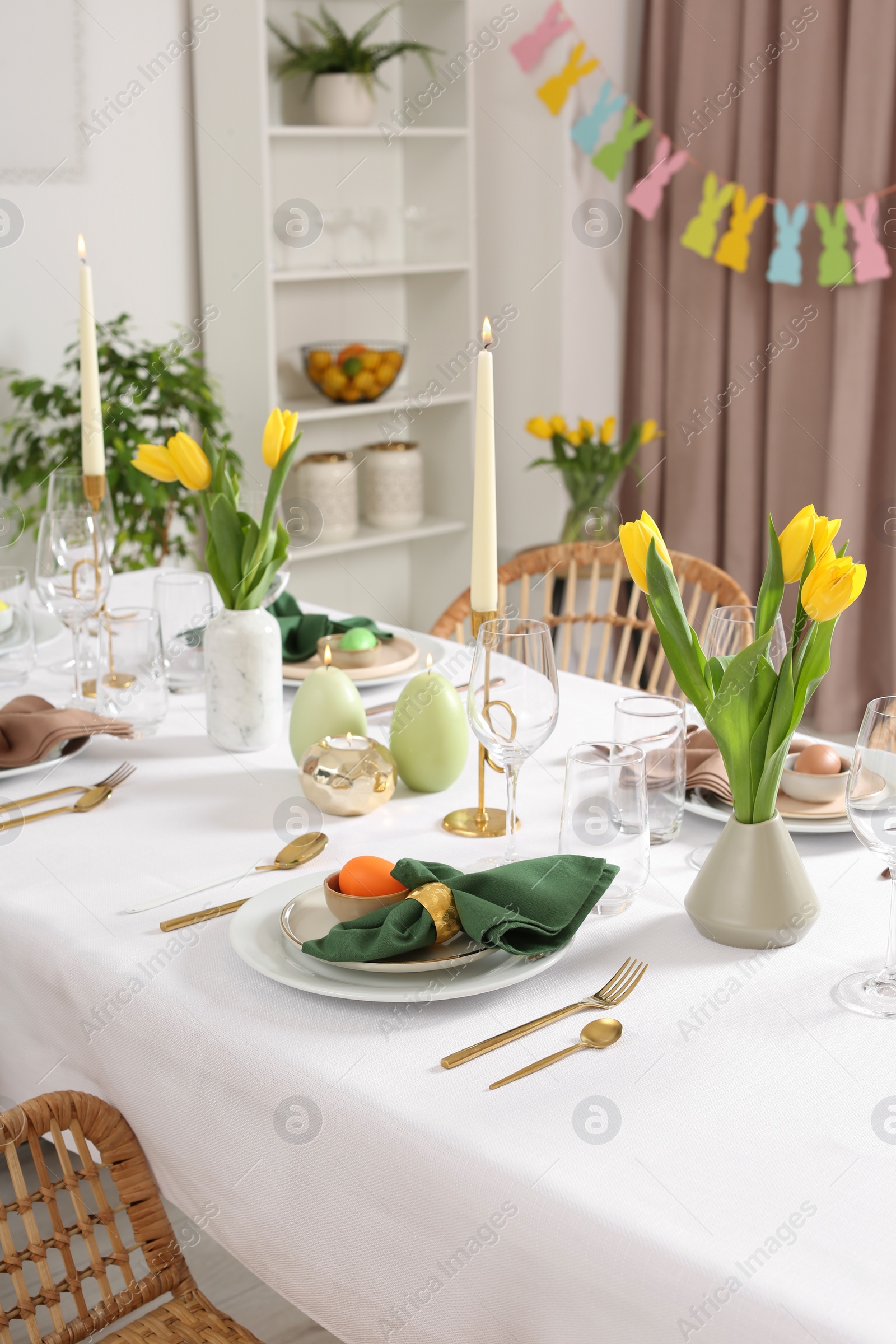 Photo of Festive Easter table setting with painted eggs, burning candles and yellow tulips in room