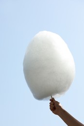 Woman holding white cotton candy against blue sky, closeup