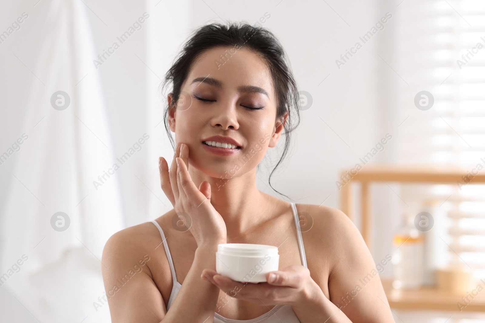 Photo of Happy woman applying face cream at home