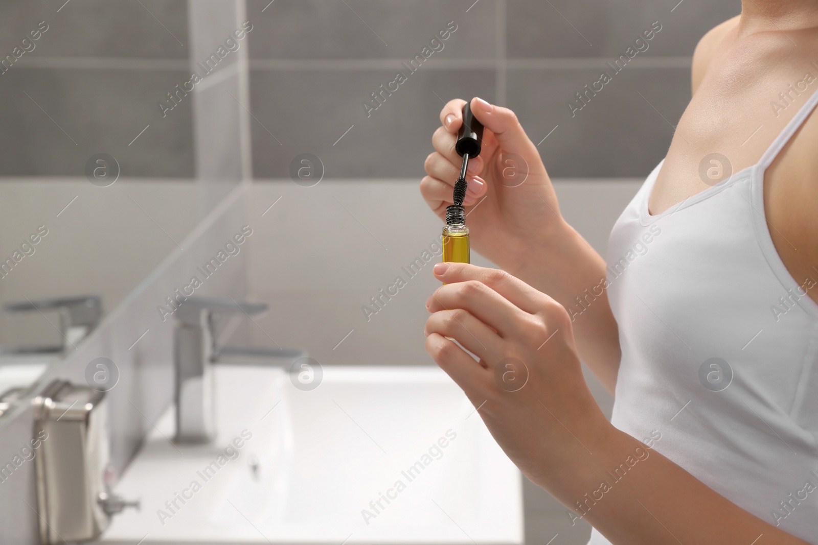 Photo of Young woman with eyelash oil in bathroom, closeup. Space for text