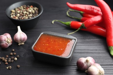 Photo of Spicy chili sauce, garlic, peppers and peppercorns on black wooden table, closeup