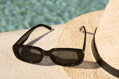 Photo of Stylish hat and sunglasses near outdoor swimming pool on sunny day, closeup