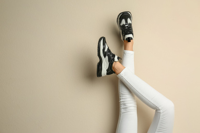 Woman wearing sneakers on beige background, closeup. Space for text