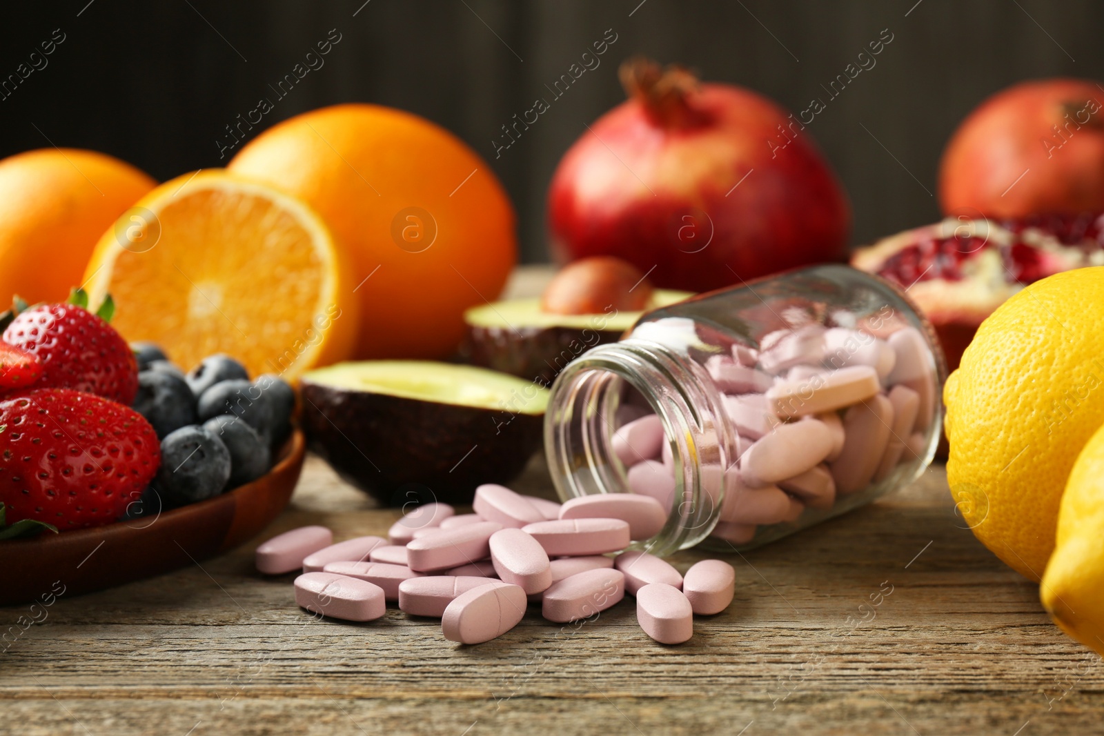 Photo of Vitamin pills in bottle and fresh fruits on wooden table