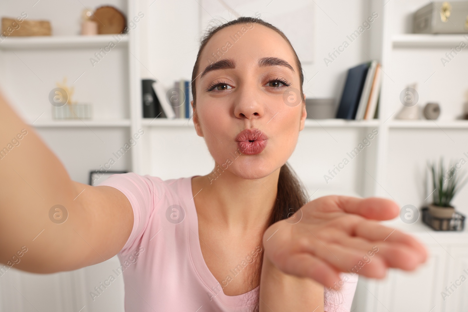 Photo of Young woman taking selfie and blowing kiss into camera at home