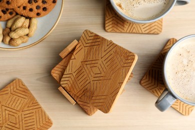 Many stylish wooden cup coasters, mugs and cookies on table, flat lay