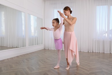 Photo of Little ballerina and her teacher practicing dance moves in studio. Space for text