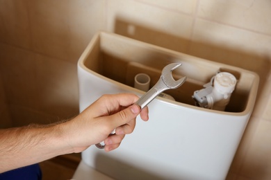 Photo of Plumber repairing toilet with wrench indoors, closeup