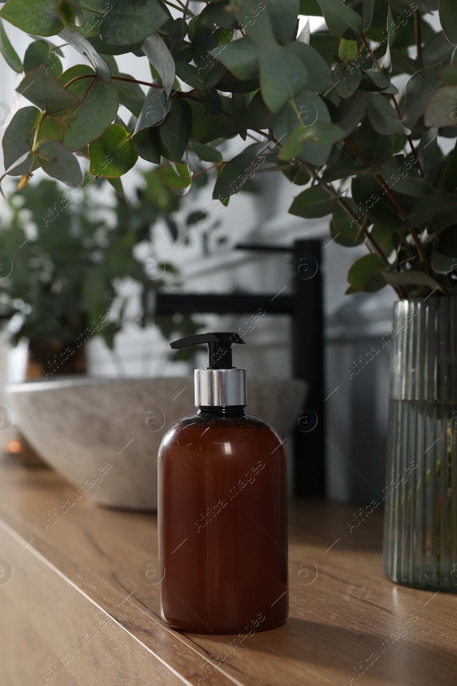 Photo of Soap bottle and eucalyptus branches near vessel sink on bathroom vanity. Interior design