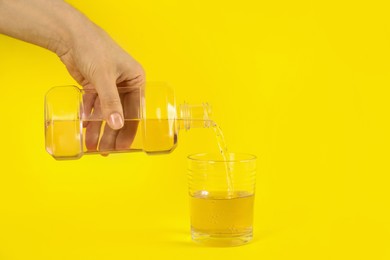 Photo of Woman pouring mouthwash into glass on yellow background, closeup