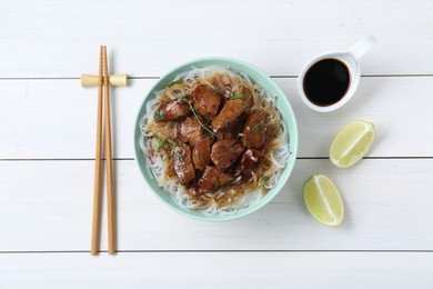 Bowl with pieces of soy sauce chicken and noodle served on white wooden table, flat lay