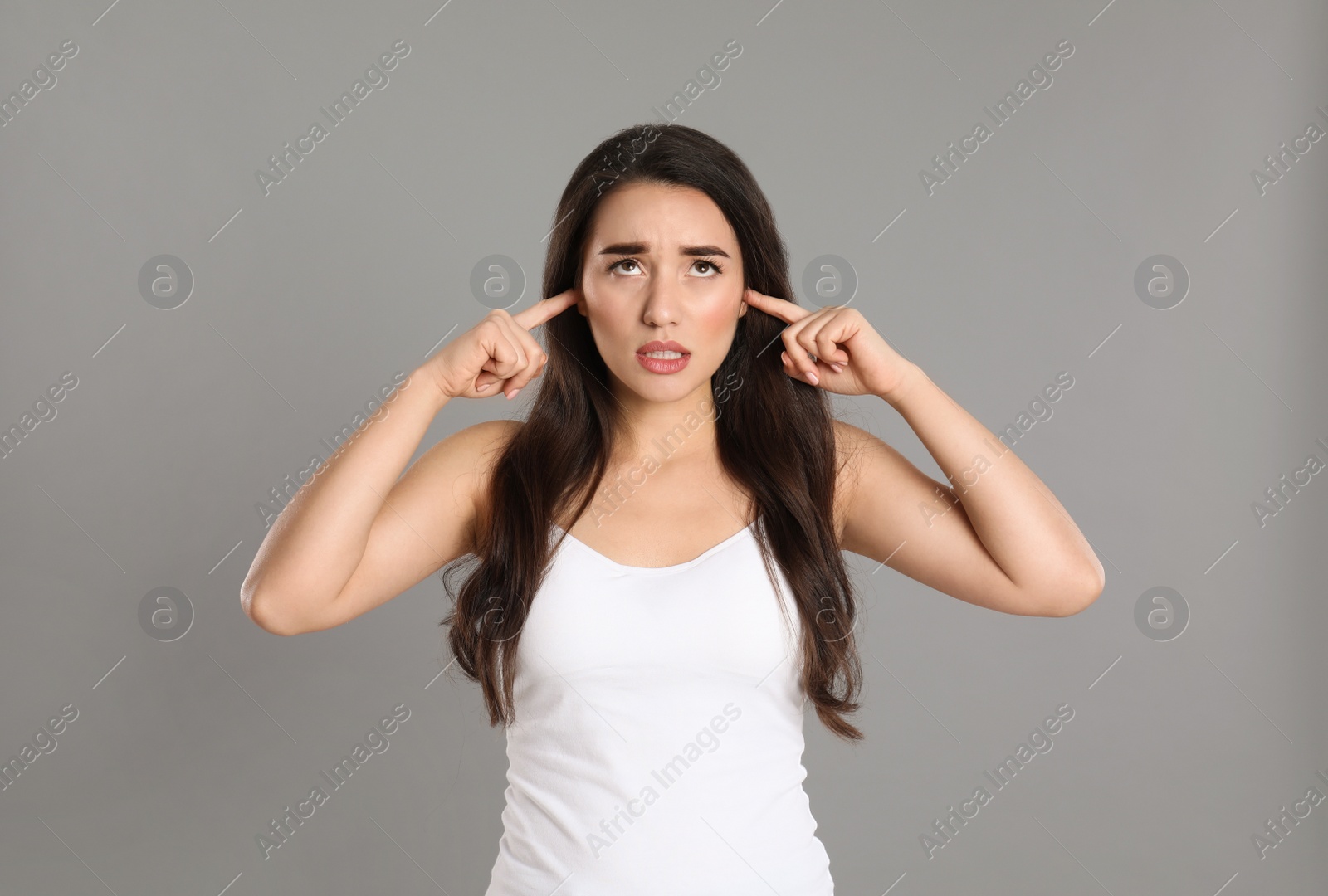 Photo of Emotional young woman covering ears with fingers on grey background