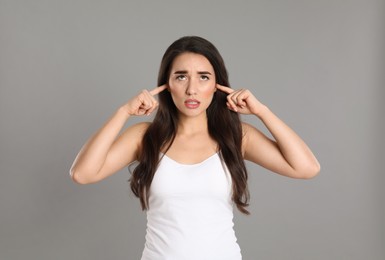 Photo of Emotional young woman covering ears with fingers on grey background