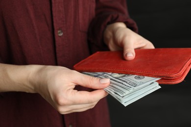 Photo of Money exchange. Woman putting dollar banknotes into wallet on dark background, closeup
