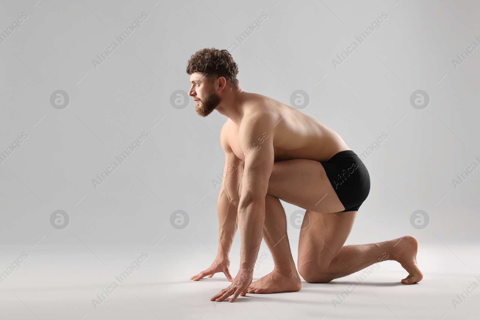 Photo of Handsome man in starting position for run on light grey background. Space for text