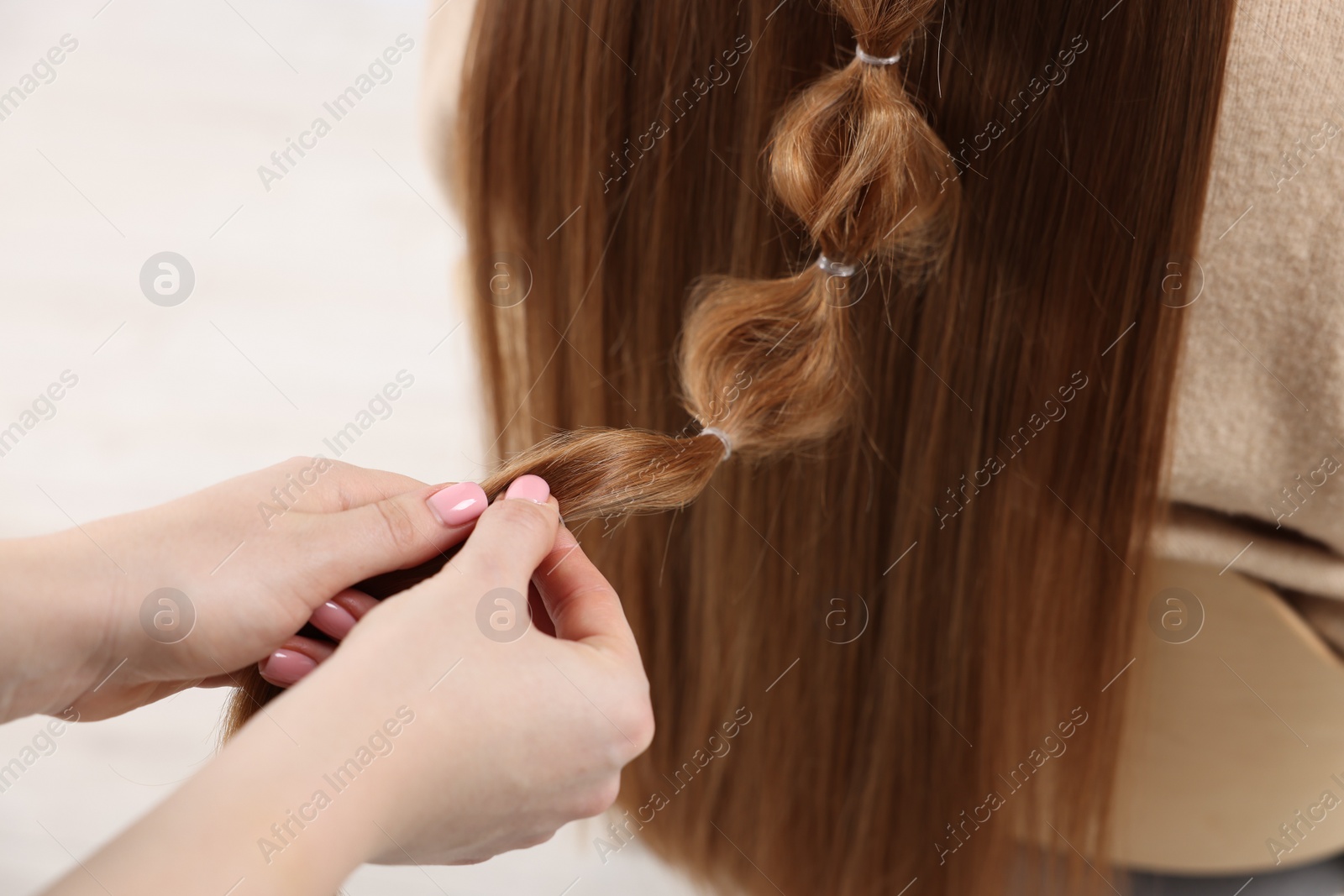 Photo of Professional stylist braiding woman's hair on blurred background, closeup