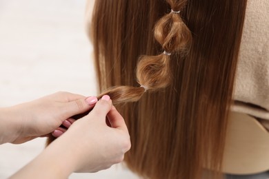 Photo of Professional stylist braiding woman's hair on blurred background, closeup