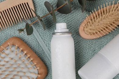 Photo of Dry shampoo sprays, hairbrushes and eucalyptus branch on towel, flat lay
