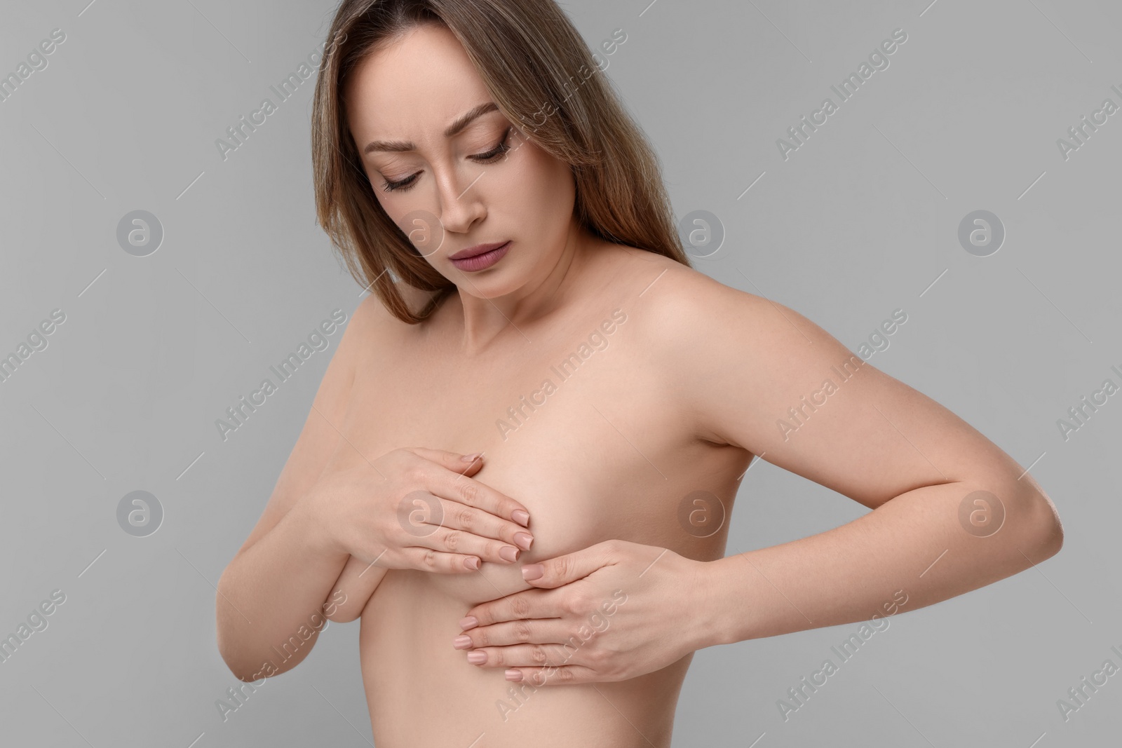 Photo of Mammology. Naked young woman doing breast self-examination on light grey background