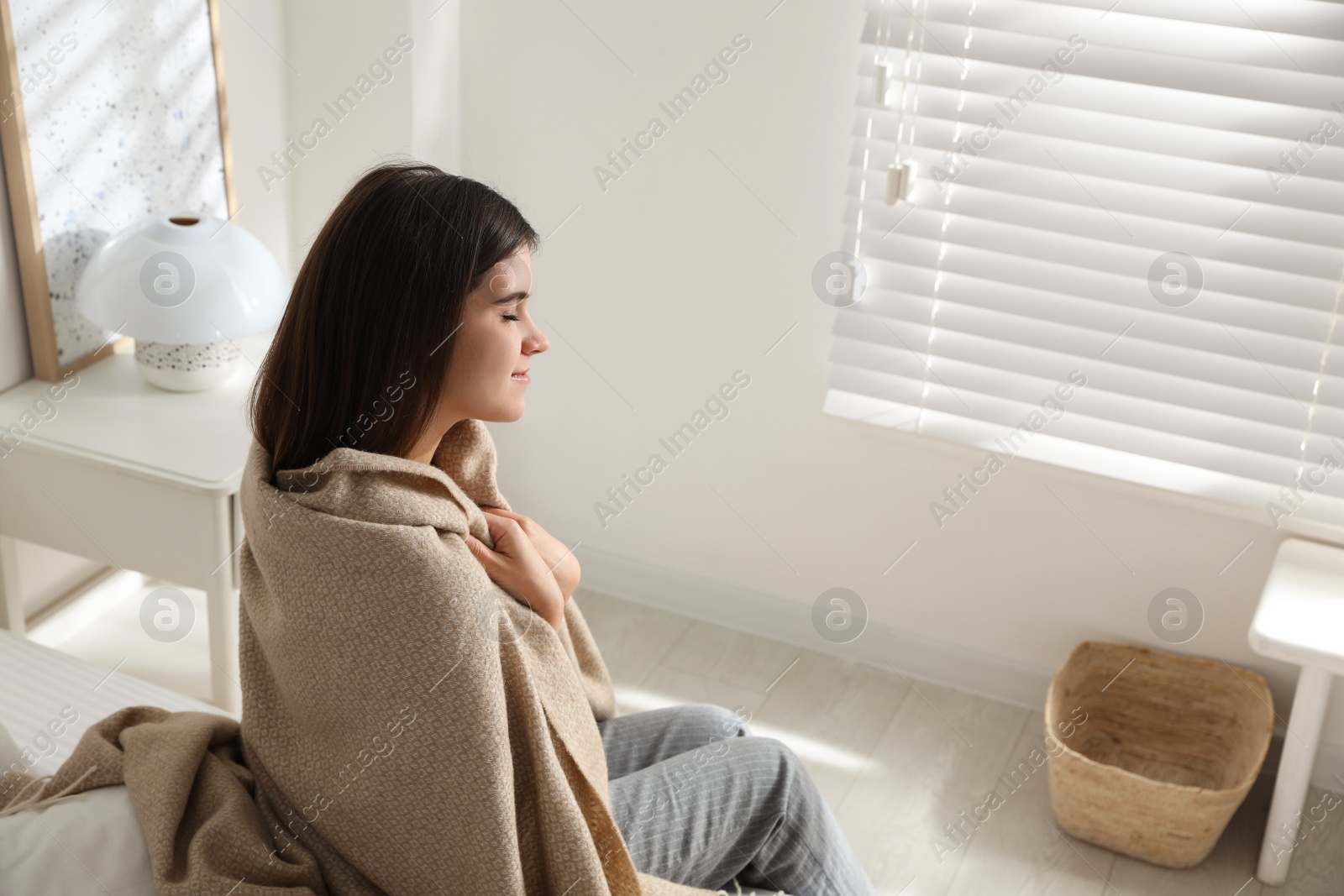 Photo of Woman covered with warm beige plaid indoors