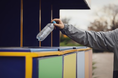Man throwing plastic bottle into garbage bin outdoors, closeup. Waste sorting