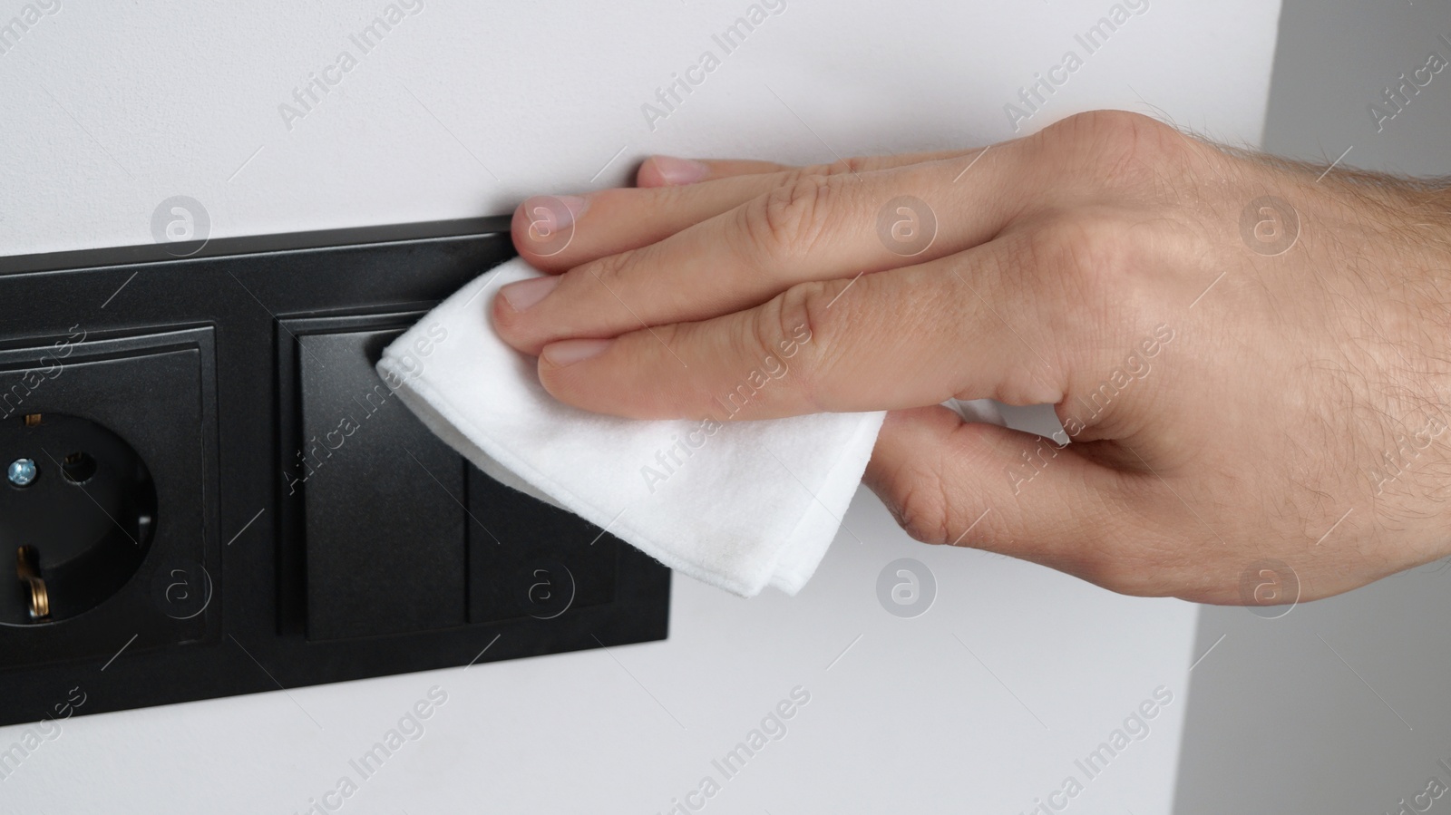 Photo of Man cleaning light switch with wet wipe indoors, closeup. Protective measures