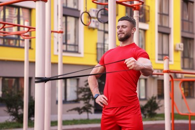 Muscular man doing exercise with elastic resistance band on sports ground