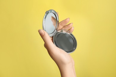 Photo of Woman holding metal cosmetic pocket mirror on yellow background, closeup