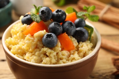 Photo of Tasty millet porridge with blueberries, pumpkin and mint in bowl on wooden table, closeup