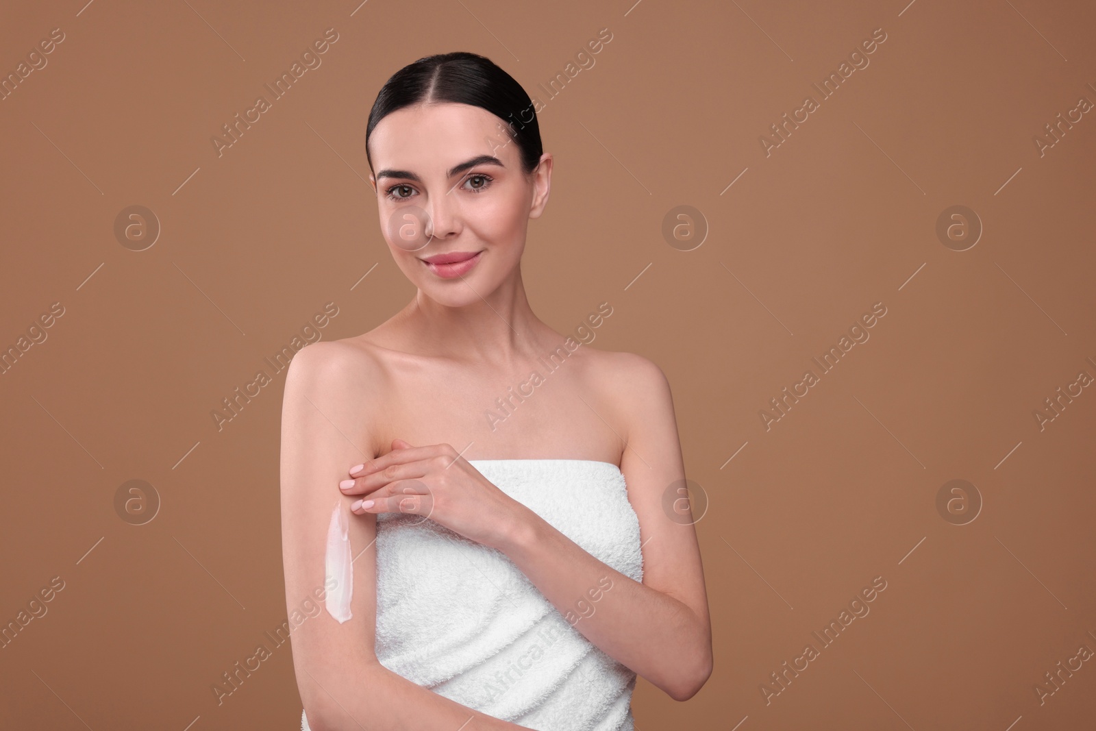 Photo of Beautiful woman with smear of body cream on her arm against light brown background