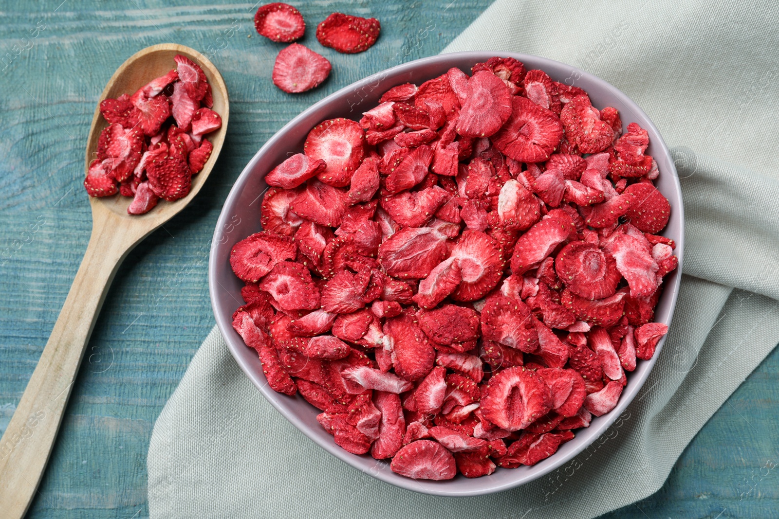 Photo of Bowl and spoon with dried strawberries on light blue wooden table, flat lay