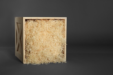 Photo of Wooden crate with shavings on dark background, space for text